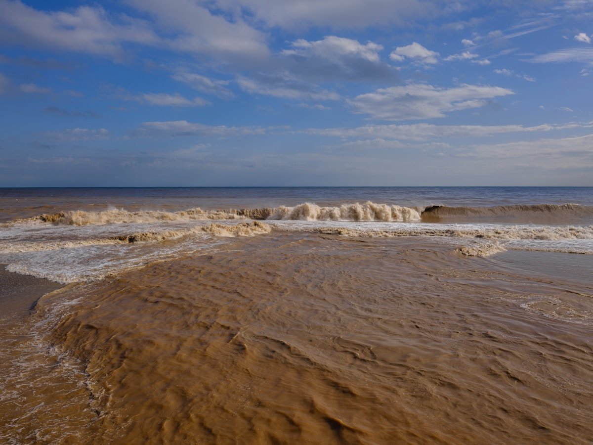 Muddy ocean waves crashing onto a sandy beach during a storm