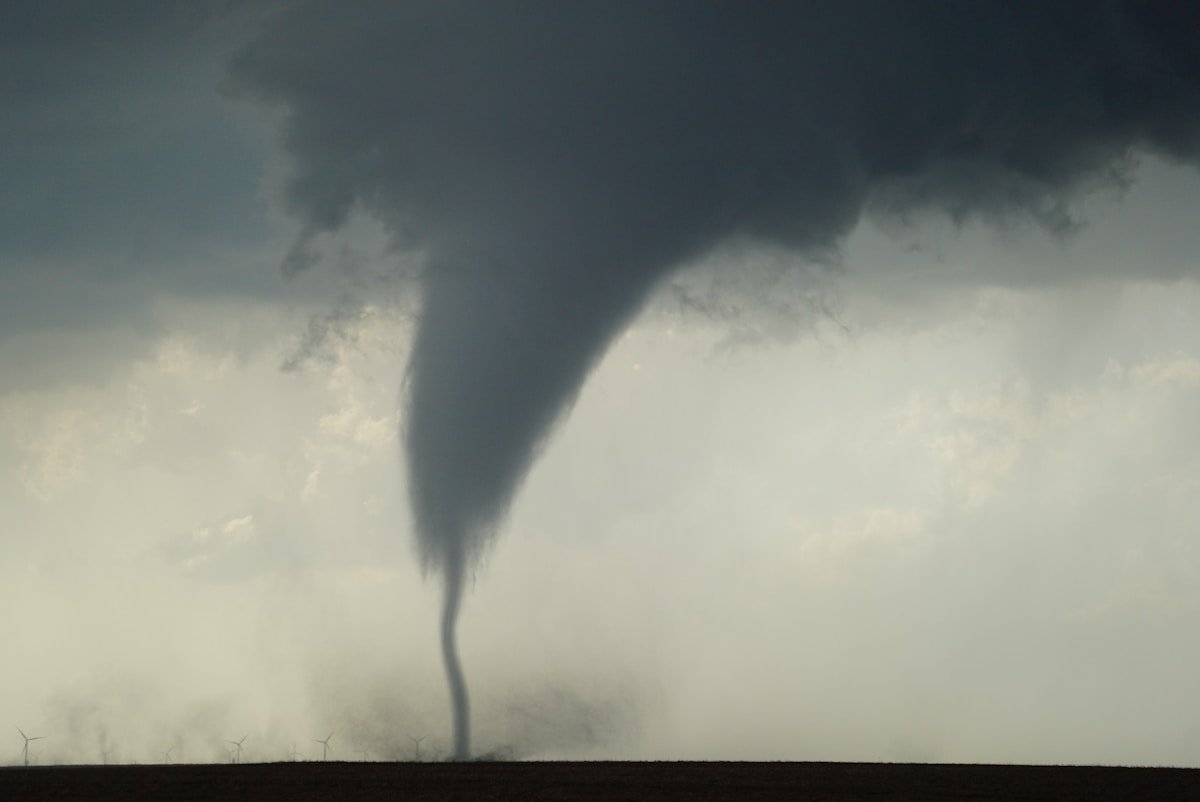Large tornado funnel cloud over rural farmland with wind turbines